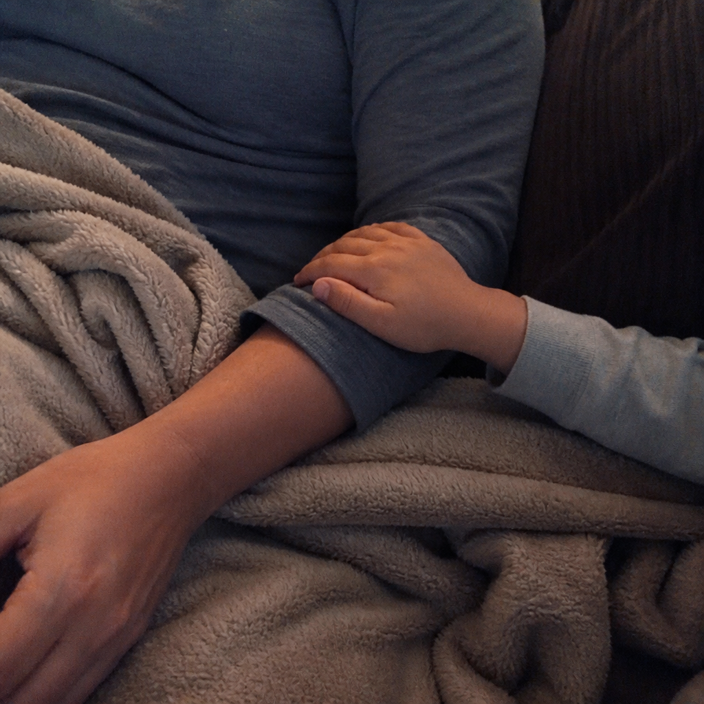 A small child's hand resting on a tired mother's arm